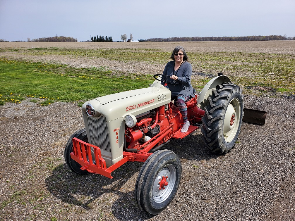 me on the tractor, wearing a grey sweater and colourful striped leggings. The tractor is an old Ford, grey and red.
