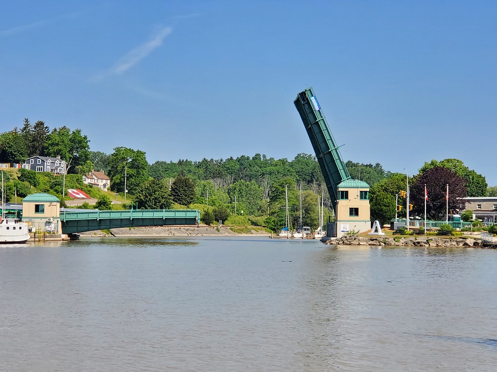 Long view of the lift bridge shows the left side down and the right side almost straight up. The sky is a perfect blue. 