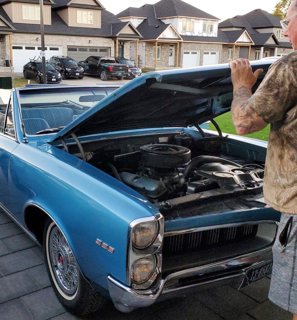 Derek opening the hood of the convertible, now in the driveway.