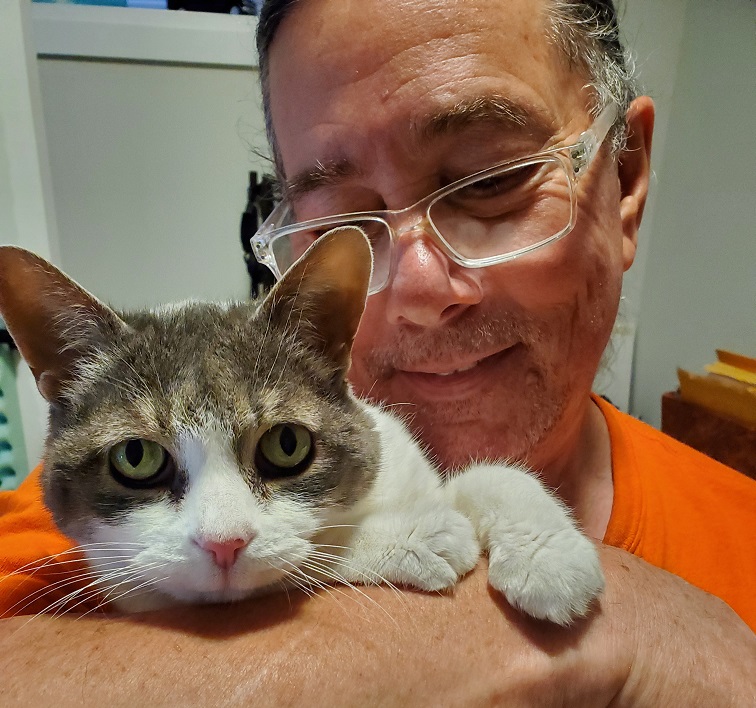 Derek and Sugar in closeup. He is holder her. She looks happy and straight into the camera. He looks adoringly at her. 