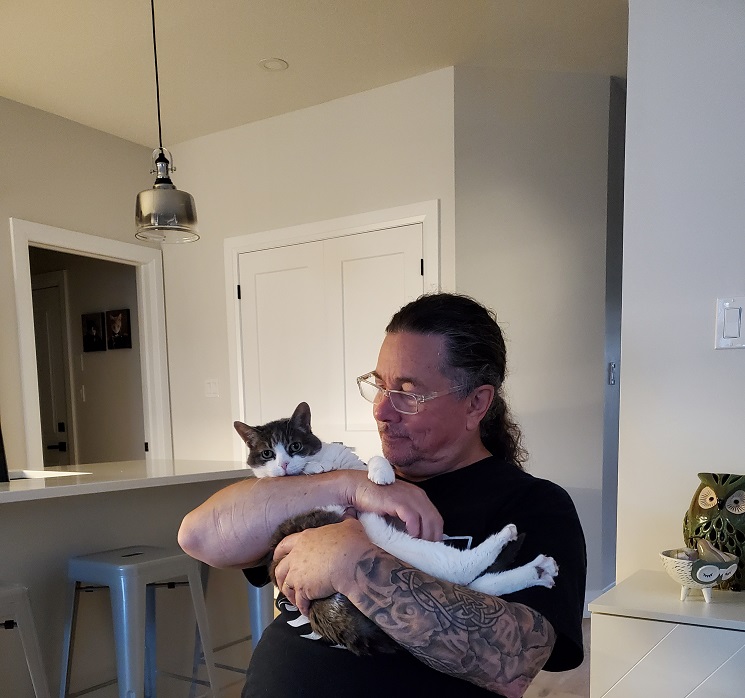 Derek smiling at Sugar who he's holding in his arms while sitting at the kitchen table.