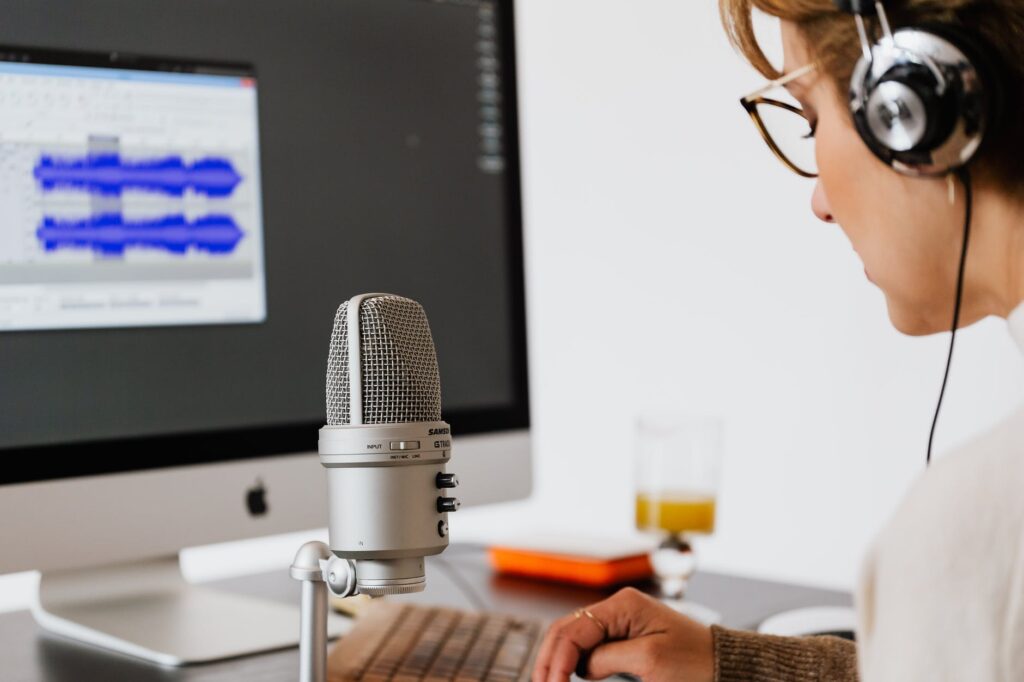 woman at desk with microphone and audio file on computer monitor in front of her