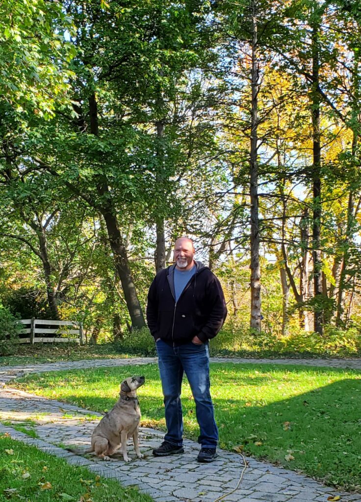 Kevin and Nacho on a paving-stone walkway with fall colours on the trees behind them