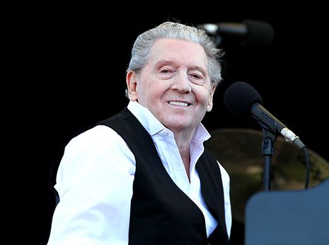 Jerry Lee Lewis in a white shirt and black vest, smiling in front of a microphone. 