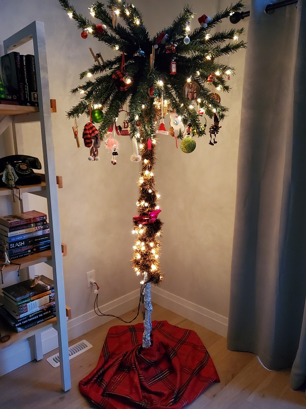 Palm style tree with clear lights and ornaments. A green, red and gold skirt is at the base. 
