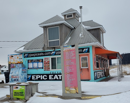 PJ's Epic Eats is a colourful building with a light blue theme, orange awning and various signs advertising smoothies and ice cream in pink and light green. 