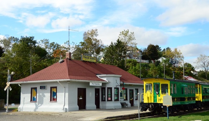 Port Stanley railway terminal with train parked beside it. Train is green and yellow.