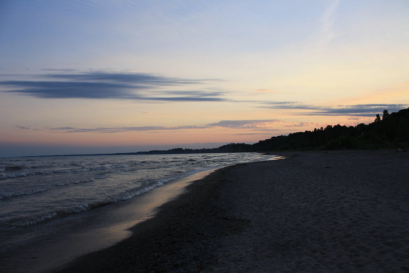 empty beach at sunset. All you can see is sand , gentle waves, and a pink sky.