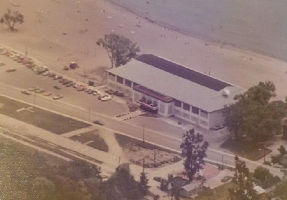 A closer view of the Stork Club from above. The parking lot is nearly full and there are people on the beach and in the water. 