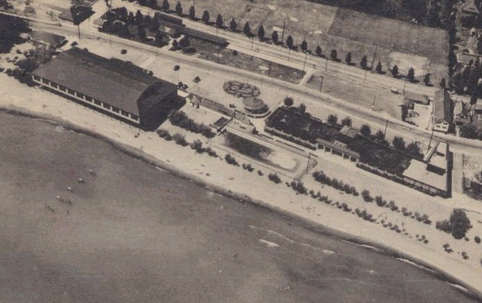 The Stork club as seen from the air. A long building with some shrubbery and a long pool, right on the lakeshore. 