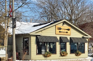 Two Forks is a light yellow building with brown striped awnings over three front windows. Two giant wooden forks are mounted horizontally over the middle window.