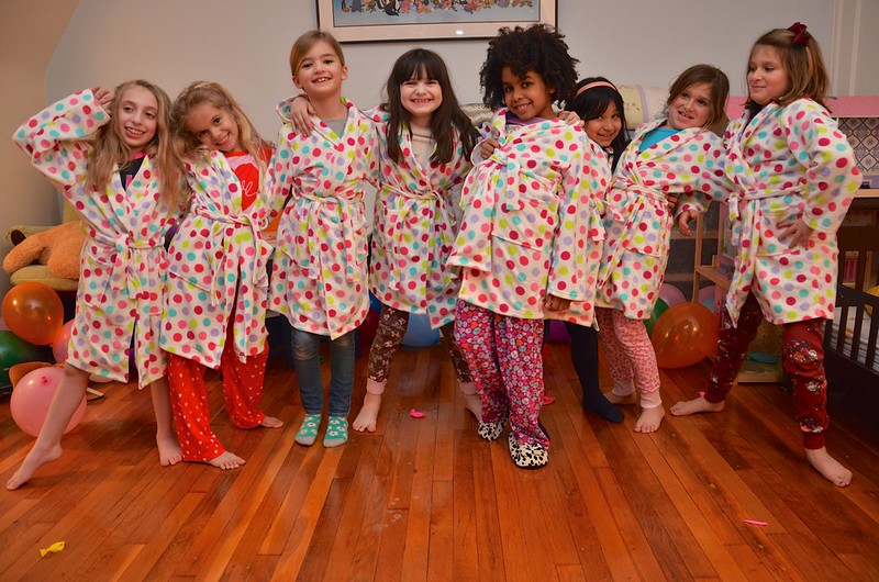 a row of little girls in matching pink robes posing at a slumber party