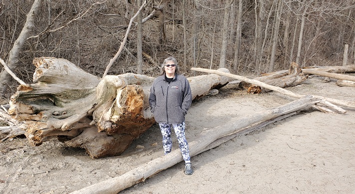 Me standing next to wood that's washed up on shore including a massive tree root that's almost as tall as me. 