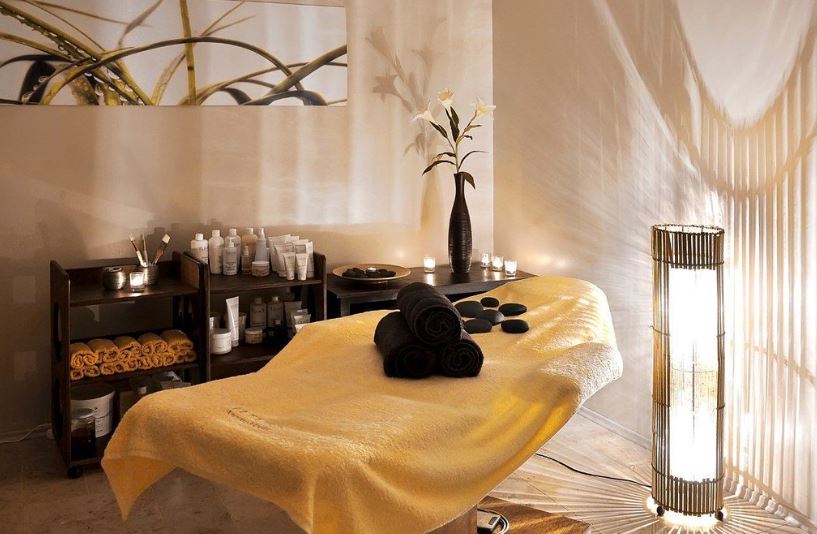 photo of a spa room with a massage table, flowers, all in hues of white and cream
