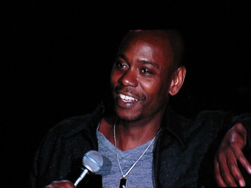 Dave Chappelle in close up, holding a mic while performing