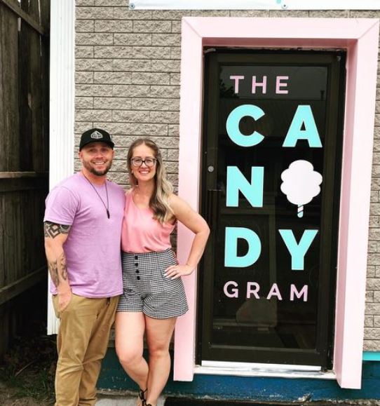 Amy and Jerry standing beside the door of their business. They are in their 30s, smiling and happy!