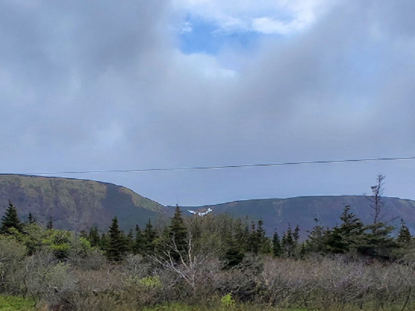 Snow lies visible in a Newfoundland valley between to large hills. A bit of blue peeks out amid the grey sky. 