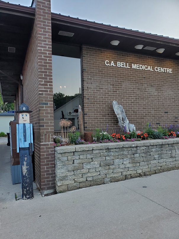 A wooden, painted police officer stands beside a brick medical building, just off the sidewalk. 