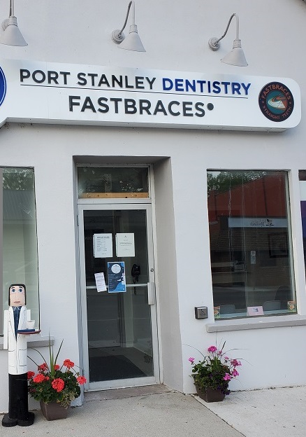 A wooden dental hygienist holds a tray with a cup and toothbrush on it as she lovingly looks across the road at Woody.