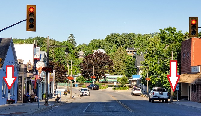 A wide perspective of Bridge Street with red and white arrows over two wooden people figures across the street from each other