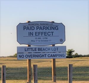 blue and white sign informs visitors to Little Beach that paid parking is in effect and no overnight camping is allowed