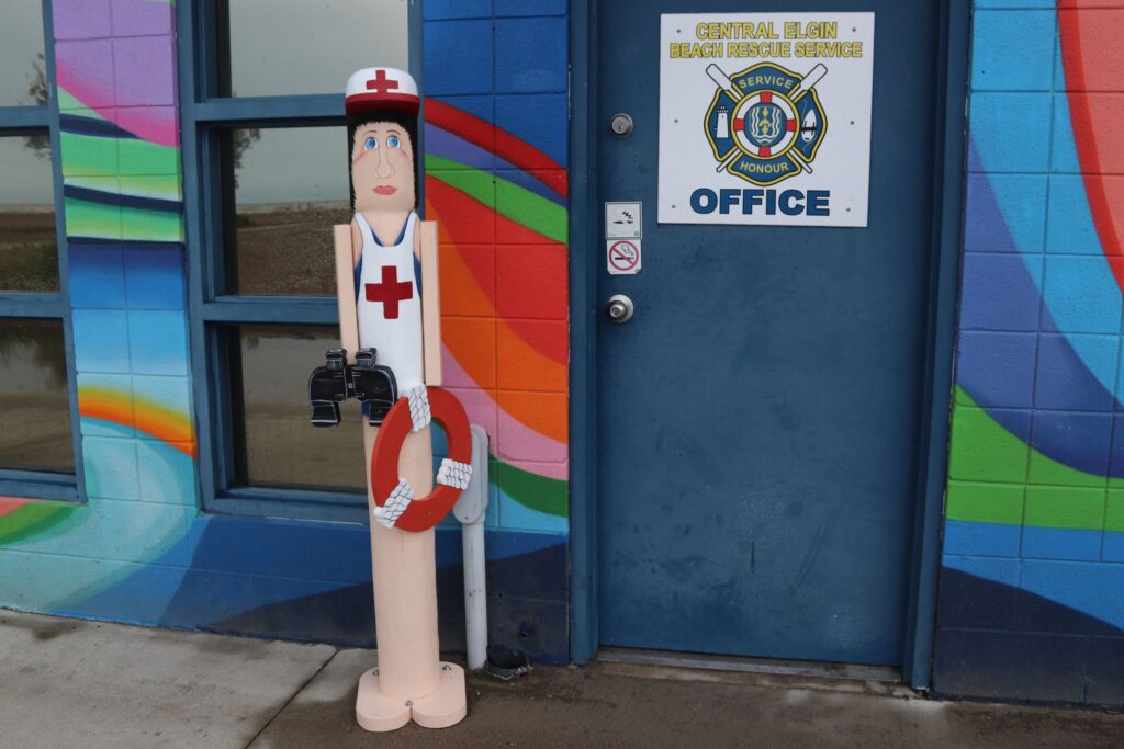 Post person with binoculars and a lifesaver outside the Central Elgin Beach Rescue service office. 