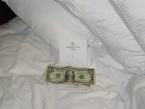 A few US bills and a note that says "for housekeeping" on an unmade hotel bed