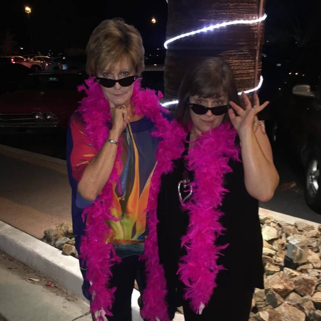 Erin and me both wearing black clothing, bright pink boas and cats-eye sunglasses outside a theatre in Palm Springs before we saw Randy Rainbow live