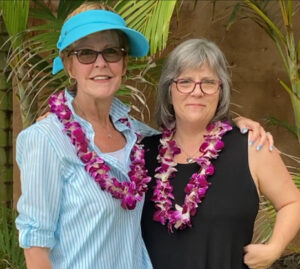 Erin and I pose in front of a palm tree while wearing live purple-flower leis around our necks