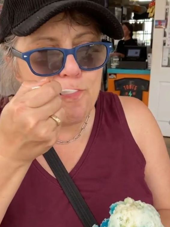 Me with a spoon in my mouth and a look of contentment on my face. You can see the shave ice in the corner. A mound of treat with yellow, blue and white colours.