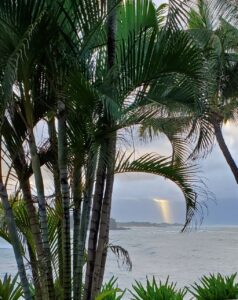 Sunlight spilling out from the clouds over the mountains in the distance with the ocean and palm trees closer
