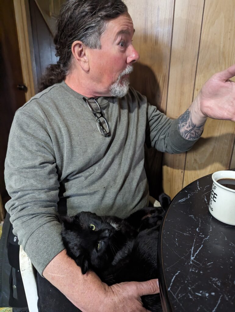 Derek in mid-story with a black cat on its back on Derek's lap. 