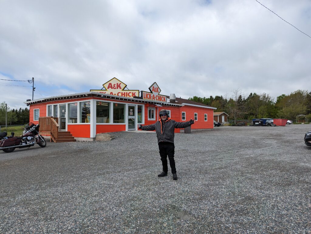 Derek in front of a big restaurant called A & K Lick-A-Chick. His Harley is off to the left in the large parking lot. 