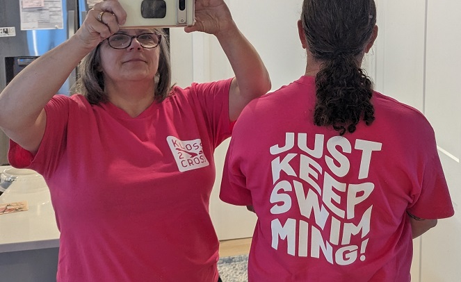 Derek and I in fuchsia t-shirts. Me facing the mirror with the Kloss 2 Kross logo on the front. Derek showing the back that reads Just Keep Swimming!