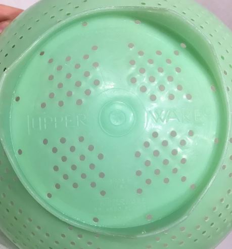 The bottom of a green, plastic colander where the word TUPPERWARE is clearly visible.