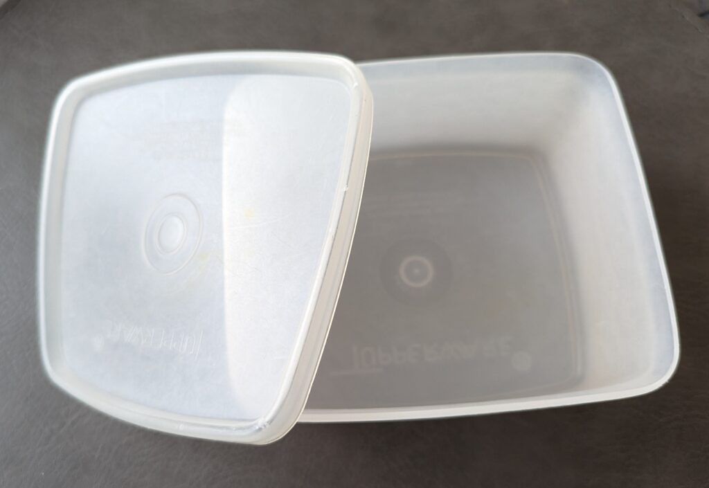 A square, white container with a lid. Both clearly say TUPPERWARE on them. 