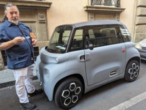 Derek stands beside a tiny, grey Citroen to demonstrate how tall it is. The top of the car is at his chest.