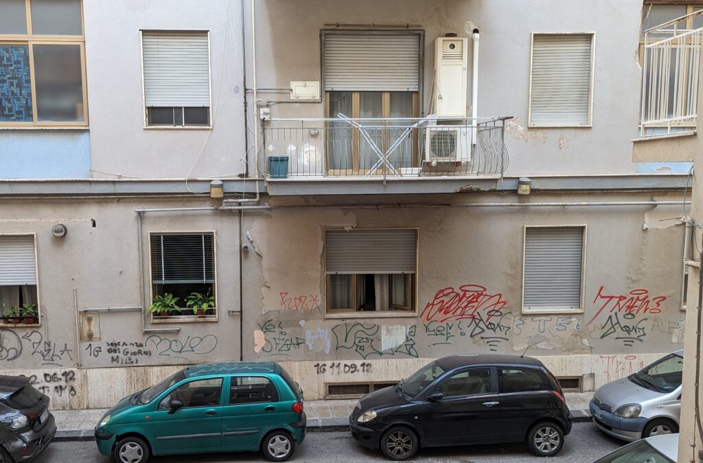 The first floor of an apartment building has graffiti all over the walls in black, green, and red spray paint. 