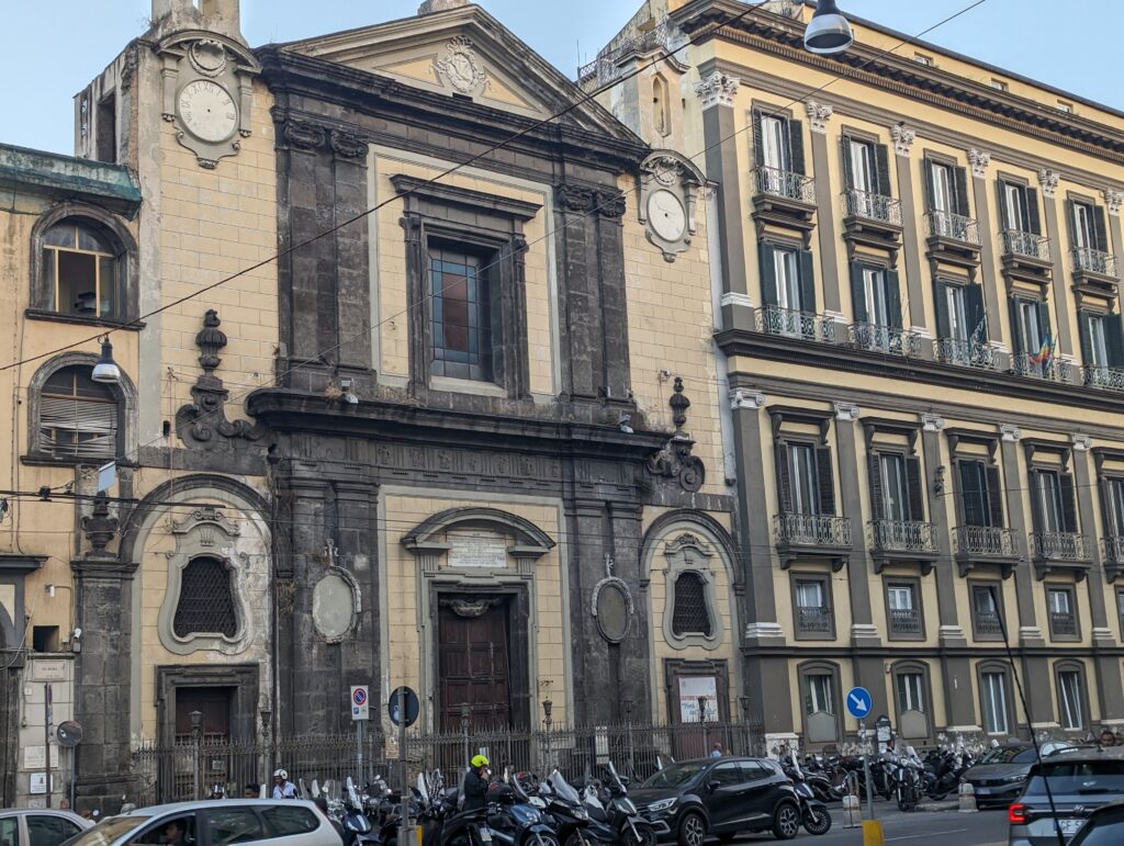 A large, beautiful building with incredible stonework in light yellow, darker, yellow, and brown. Also pillars and iron balcony railings as well as stained-glass windows. 