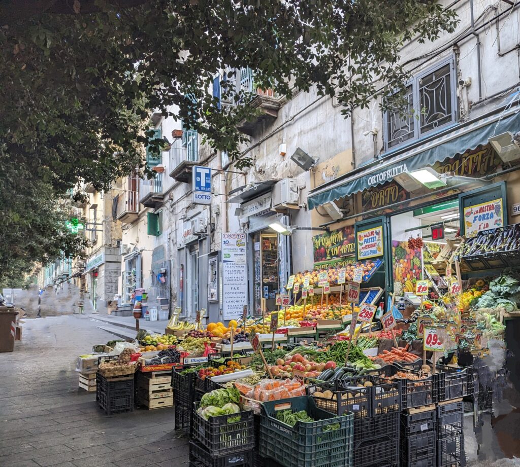 A fruit and vegetable shop in Naples with all kinds of produce out on the walkway in plastic bins and crates. 