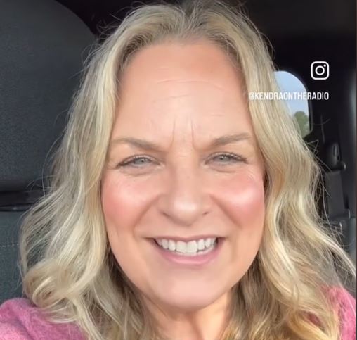 Close-up of Kendra smiling. She has long blond hair and is wearing pink