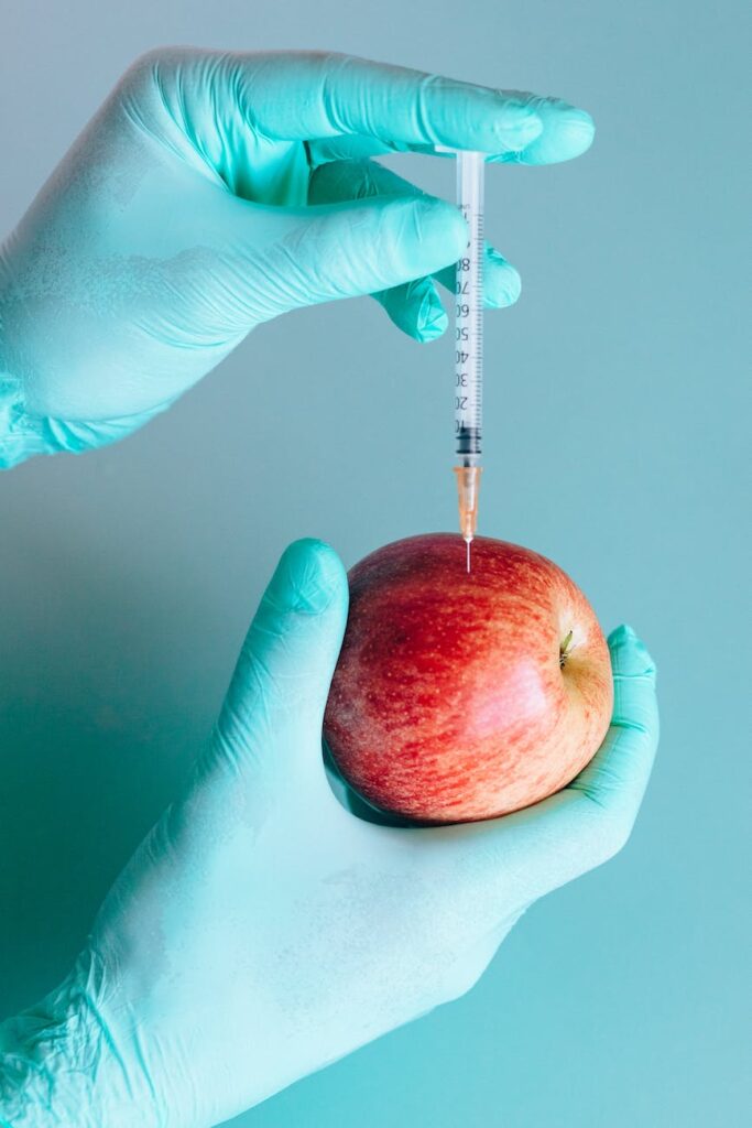 person injecting a red apple by using a syringe