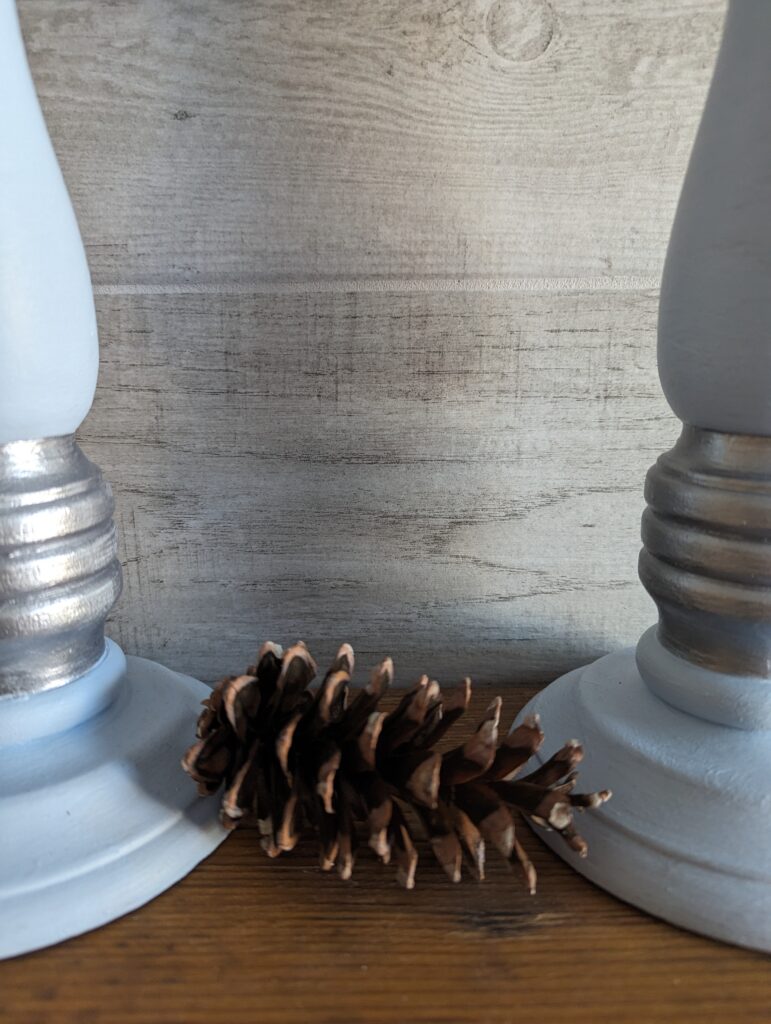 An ordinary pinecone sits between the bases of two light blue candlesticks.