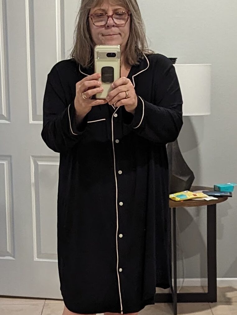 A full length selfie of me, wearing a long, black sleepshirt with white piping and buttons. 