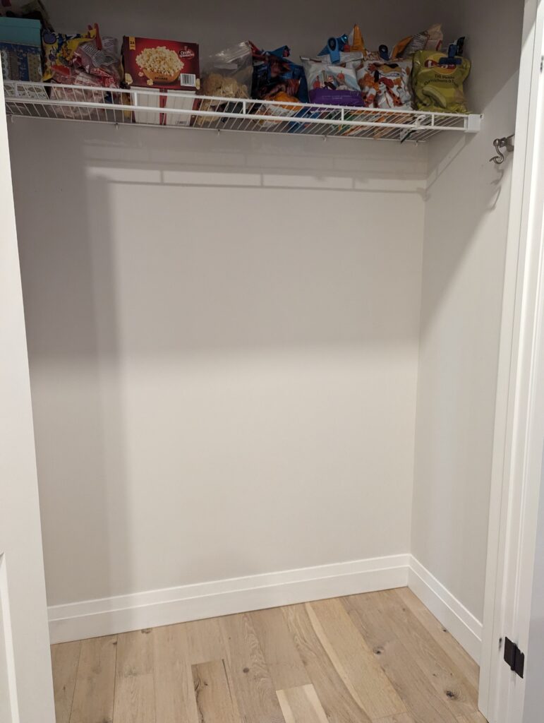 The space is completely bare except for a box of microwave popcorn and bags of chips in a row, on a wire shelf above where the bookshelf was.