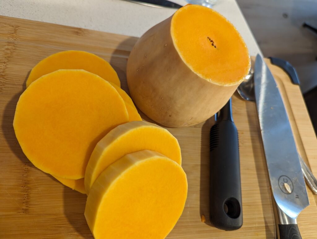 Sliced and peeled butternut squash on a cutting board beside a large knife.