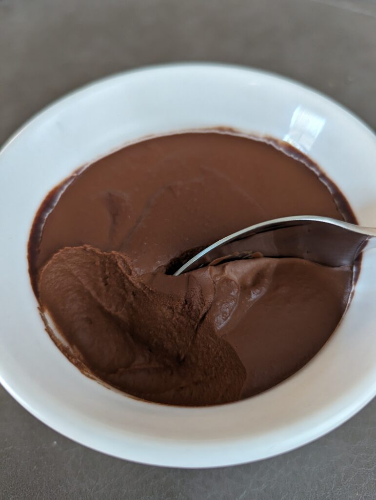 White ramekin with a spoon in the dark brown pudding that looks thick and smooth.