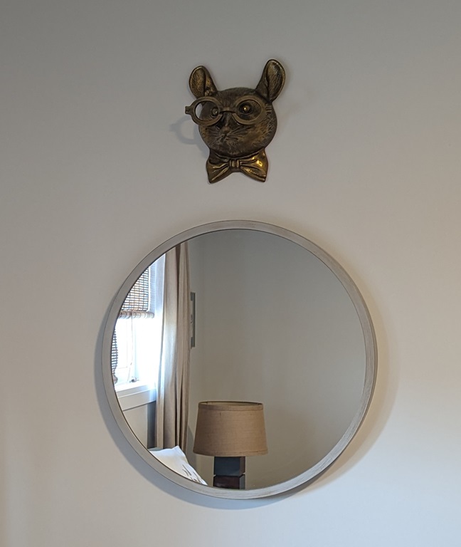 Brass mouse head above a mirror. The mouse is wearing a bow tie and glasses.
