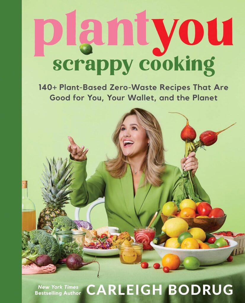 Cover of Scrappy Cooking. Carleigh is tossing an apple into the air, wearing a green jacket in front of a lighter green background with all sorts of fresh food in front of her.