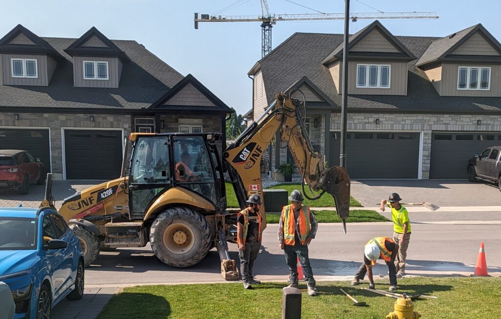 A work crew of five in front of our house with a large machine that has a jackhammer on the front of it.